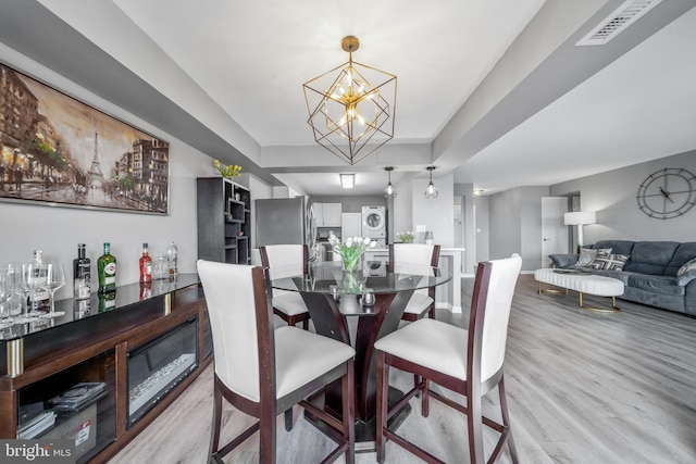 dining space featuring a notable chandelier, stacked washer / dryer, visible vents, light wood-style floors, and a tray ceiling