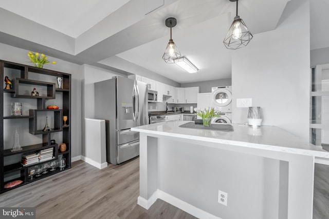 kitchen with stacked washer and dryer, decorative light fixtures, a peninsula, stainless steel appliances, and white cabinetry