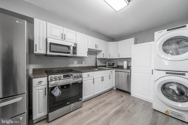 kitchen with dark countertops, appliances with stainless steel finishes, stacked washing maching and dryer, and white cabinetry