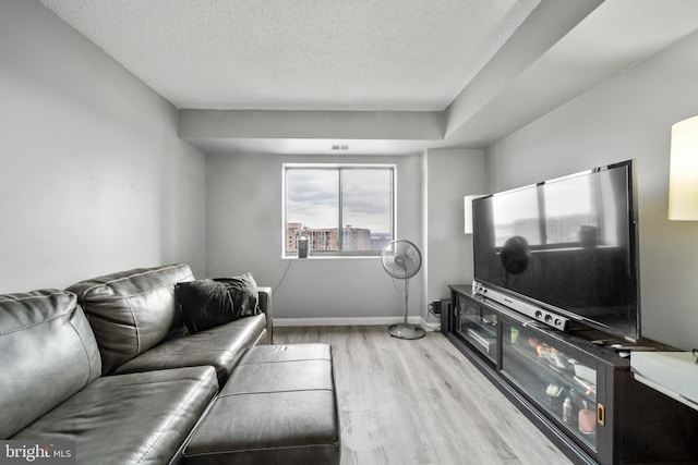 living room featuring light wood-style floors, visible vents, baseboards, and a textured ceiling