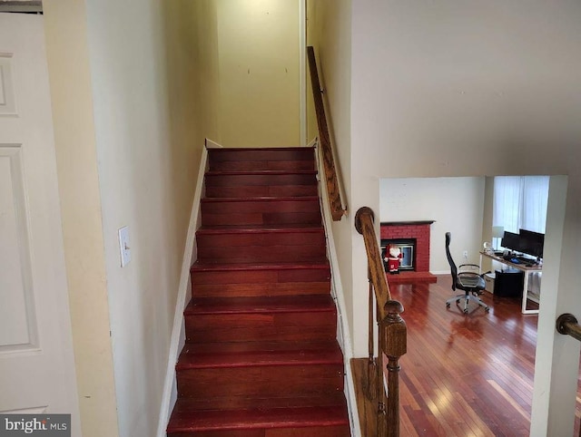 staircase featuring a brick fireplace and wood-type flooring