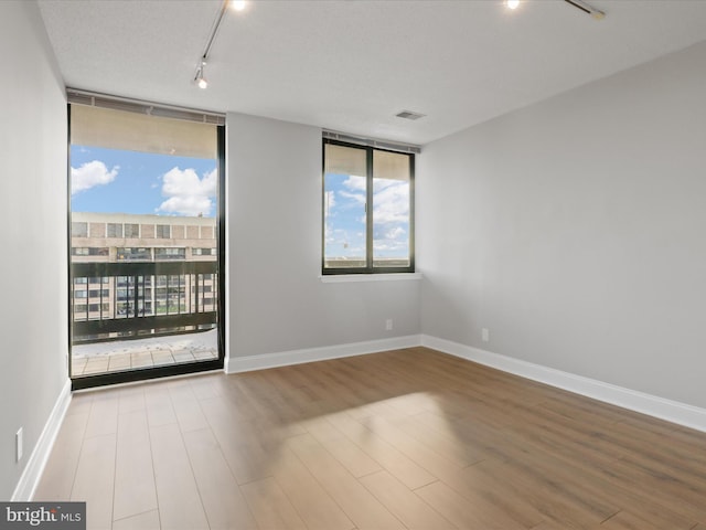 empty room with hardwood / wood-style flooring, a textured ceiling, and track lighting