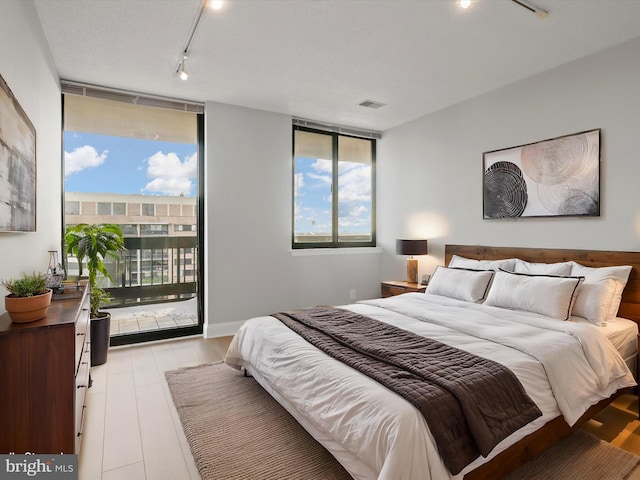 bedroom featuring access to outside, a textured ceiling, track lighting, and light wood-type flooring