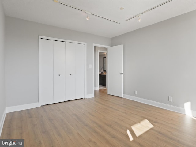 unfurnished bedroom featuring a closet, track lighting, and light hardwood / wood-style flooring