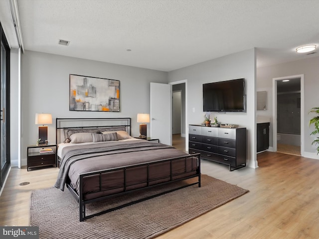 bedroom with ensuite bathroom, light hardwood / wood-style floors, and a textured ceiling