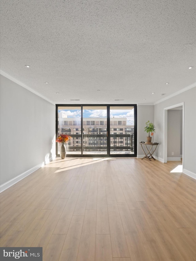 spare room featuring expansive windows, ornamental molding, a textured ceiling, and light hardwood / wood-style flooring