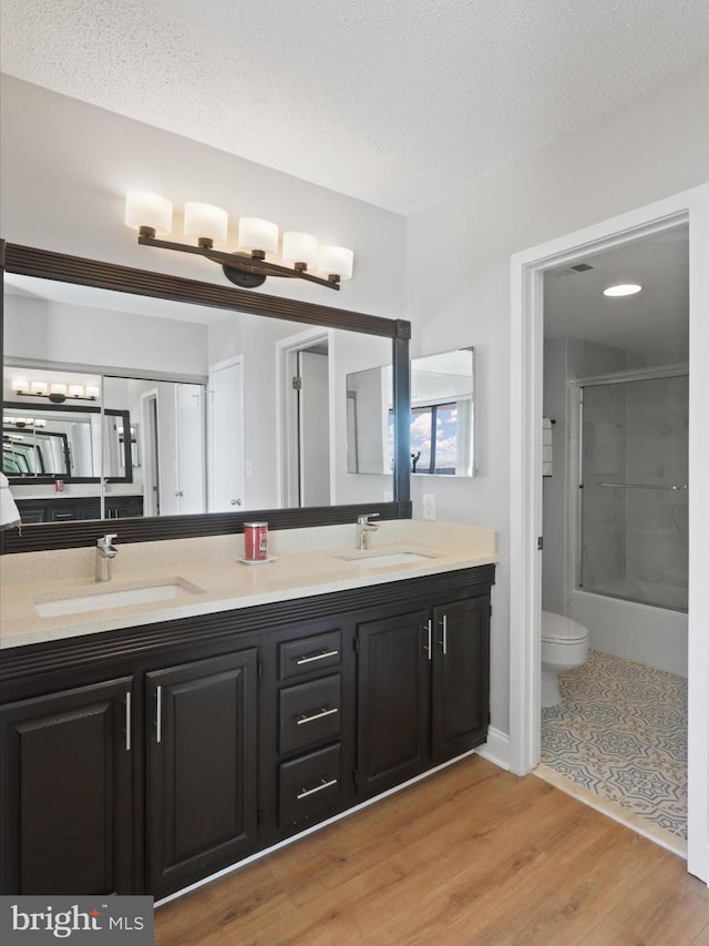 full bathroom with a textured ceiling, toilet, shower / bath combination with glass door, vanity, and hardwood / wood-style flooring