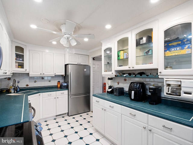 kitchen featuring sink, decorative backsplash, stainless steel fridge, ceiling fan, and white cabinetry