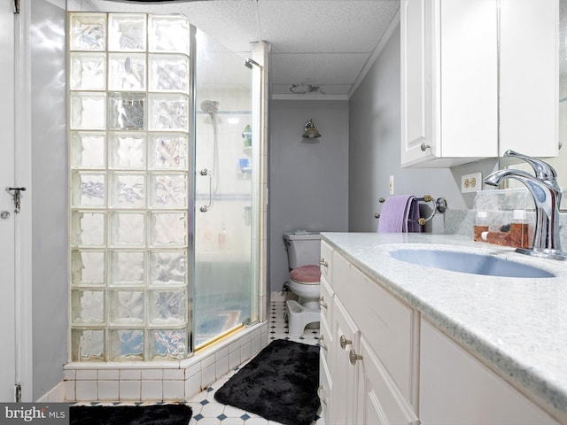 bathroom featuring vanity, toilet, walk in shower, and a paneled ceiling