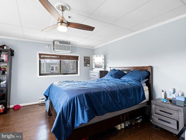 bedroom with ceiling fan, a wall mounted air conditioner, dark hardwood / wood-style floors, a baseboard heating unit, and a paneled ceiling