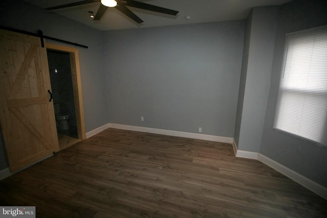 unfurnished bedroom with a barn door, ensuite bathroom, dark hardwood / wood-style flooring, and ceiling fan