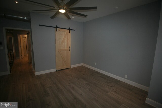 unfurnished bedroom with a barn door, ceiling fan, and dark wood-type flooring