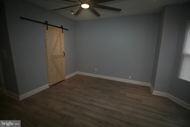 empty room featuring a barn door, ceiling fan, and dark hardwood / wood-style floors