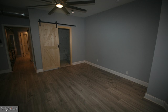 unfurnished bedroom with ceiling fan, a barn door, and dark hardwood / wood-style floors