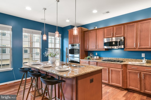 kitchen featuring an island with sink, light hardwood / wood-style floors, decorative light fixtures, and appliances with stainless steel finishes