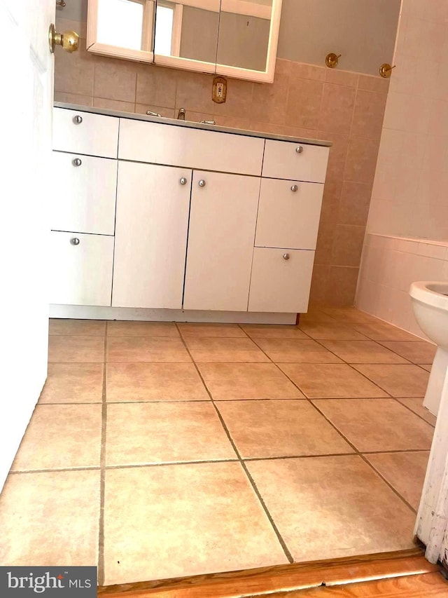 bathroom with toilet, vanity, tile patterned floors, and tile walls