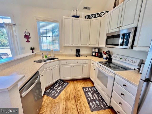 kitchen with sink, stainless steel appliances, kitchen peninsula, white cabinets, and light wood-type flooring