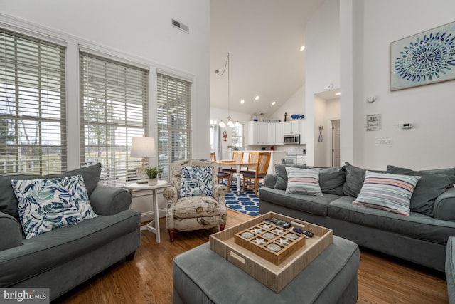 living room featuring wood-type flooring, high vaulted ceiling, and a notable chandelier