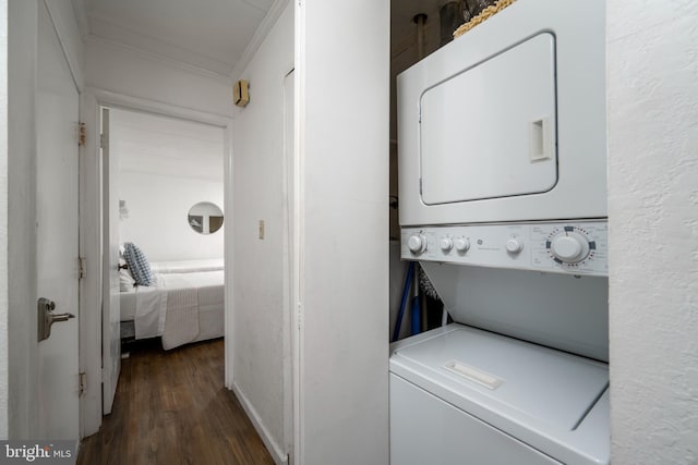 laundry area with dark wood-type flooring, ornamental molding, and stacked washer / drying machine