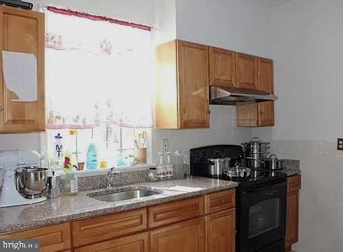 kitchen with light stone counters, a sink, brown cabinets, black electric range, and under cabinet range hood