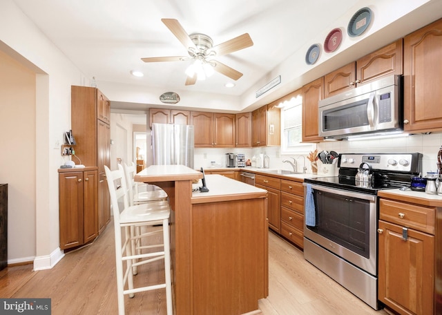 kitchen with a kitchen bar, backsplash, stainless steel appliances, light hardwood / wood-style floors, and a kitchen island