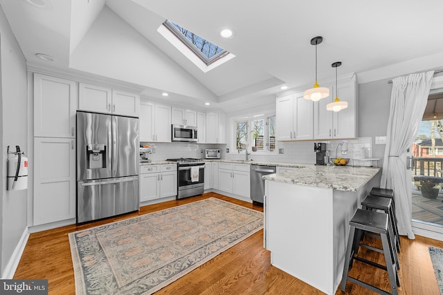 kitchen with white cabinetry, hanging light fixtures, stainless steel appliances, a kitchen bar, and kitchen peninsula