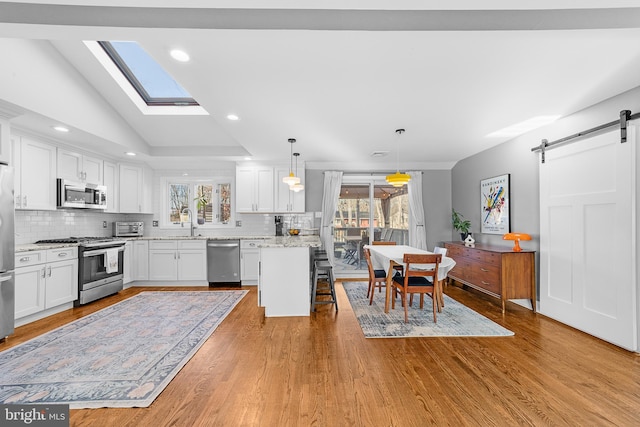 kitchen featuring stainless steel appliances, white cabinetry, a barn door, and decorative light fixtures