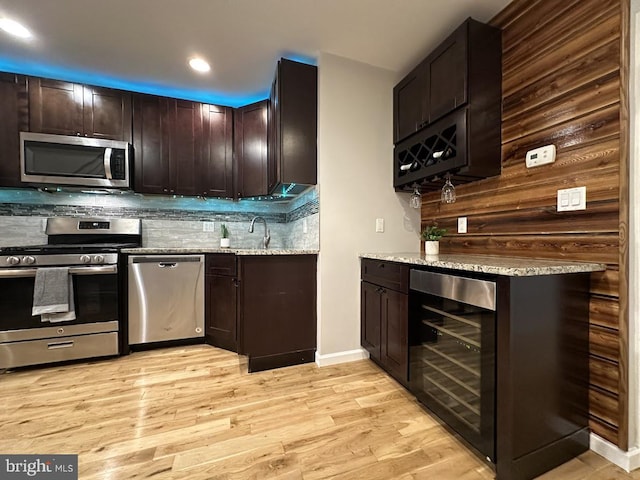 kitchen with appliances with stainless steel finishes, dark brown cabinets, light stone counters, and beverage cooler