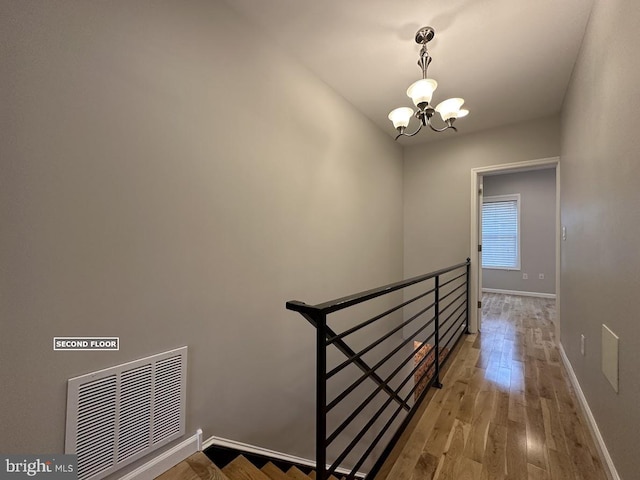 stairs with hardwood / wood-style floors and a notable chandelier