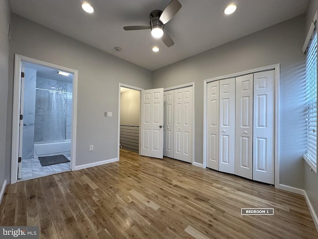 unfurnished bedroom featuring ensuite bathroom, ceiling fan, light hardwood / wood-style floors, and two closets