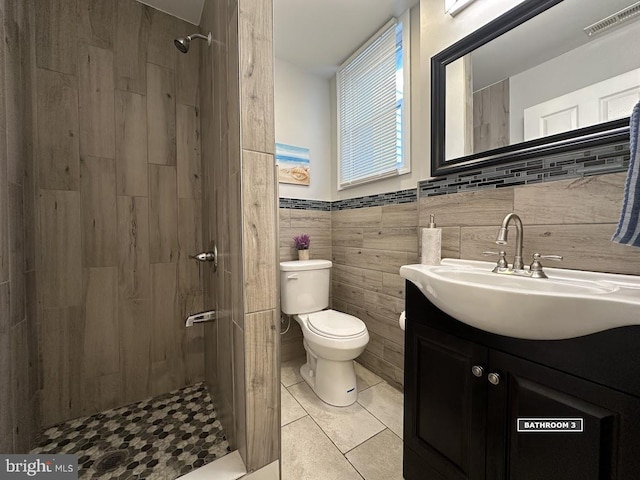 bathroom with tile patterned floors, a tile shower, vanity, tile walls, and toilet