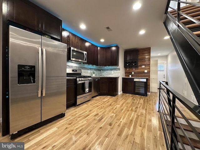 kitchen featuring light stone countertops, decorative backsplash, dark brown cabinets, stainless steel appliances, and light hardwood / wood-style flooring