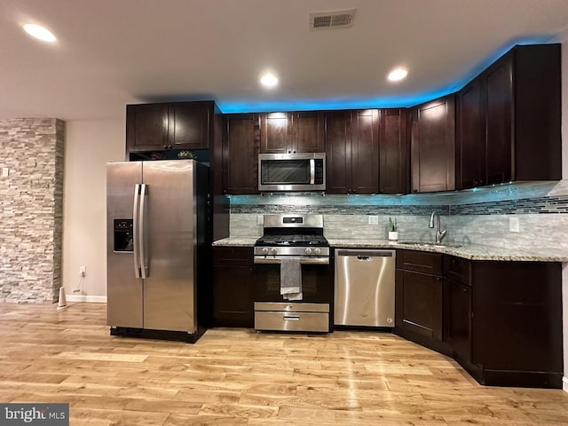 kitchen featuring appliances with stainless steel finishes, light stone counters, dark brown cabinetry, sink, and light hardwood / wood-style floors