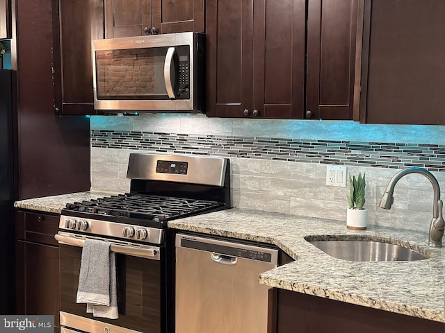 kitchen featuring backsplash, light stone countertops, sink, and appliances with stainless steel finishes