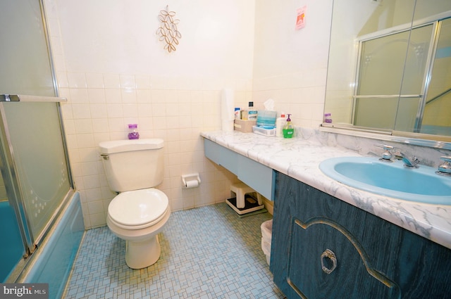 full bathroom featuring combined bath / shower with glass door, vanity, tile walls, tile patterned flooring, and toilet