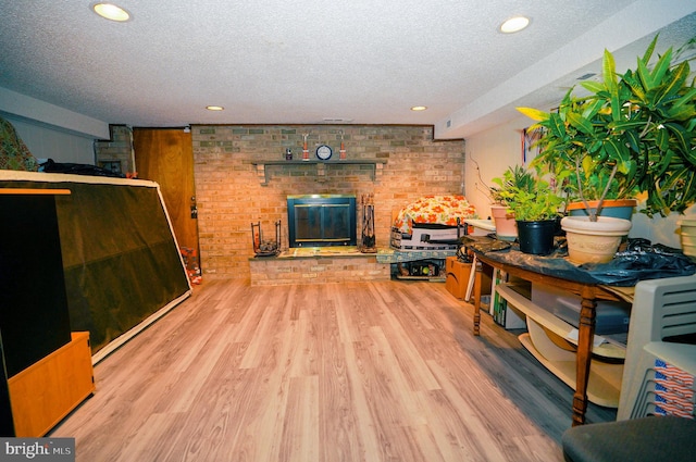 living room featuring hardwood / wood-style flooring, a textured ceiling, brick wall, and a brick fireplace