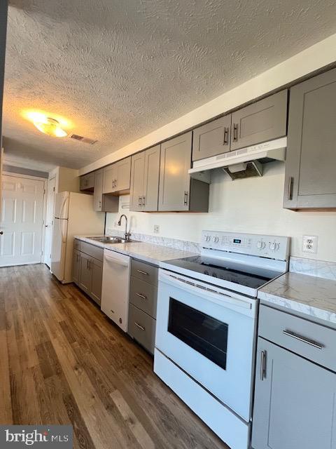 kitchen featuring light stone countertops, sink, dark hardwood / wood-style flooring, white appliances, and gray cabinets