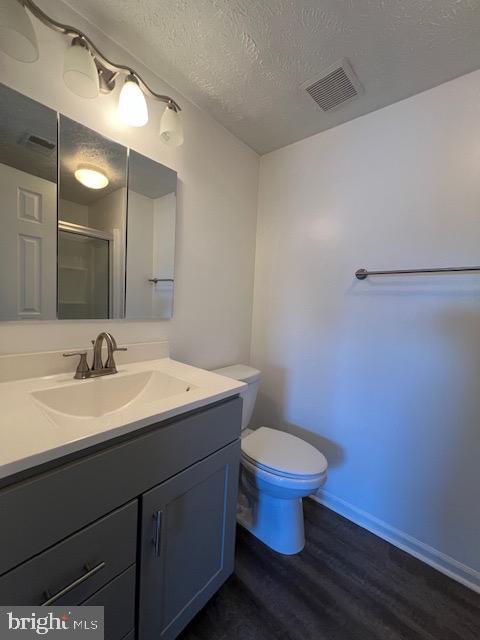 bathroom with vanity, a textured ceiling, hardwood / wood-style flooring, toilet, and a shower with shower door