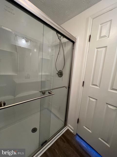 bathroom with a textured ceiling, hardwood / wood-style flooring, and a shower with shower door