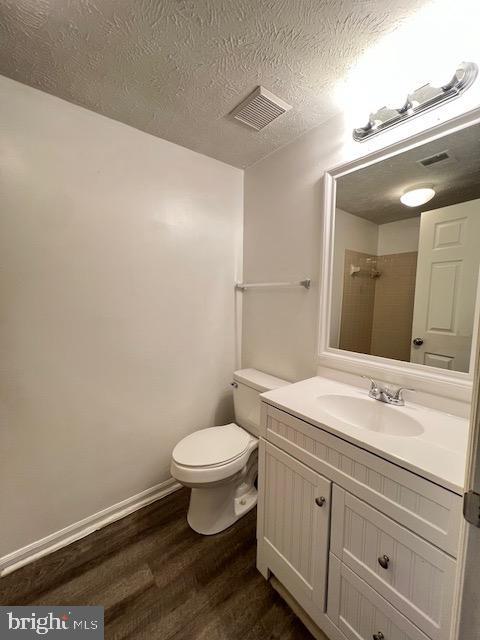 bathroom with walk in shower, vanity, a textured ceiling, wood-type flooring, and toilet