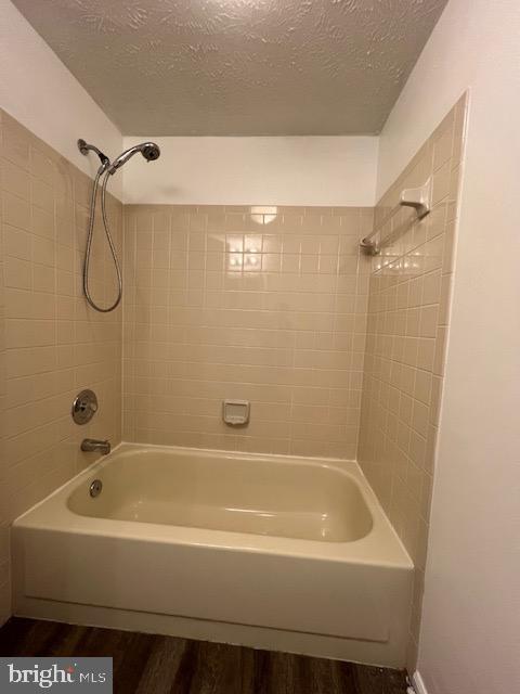 bathroom featuring hardwood / wood-style flooring, a textured ceiling, and tiled shower / bath