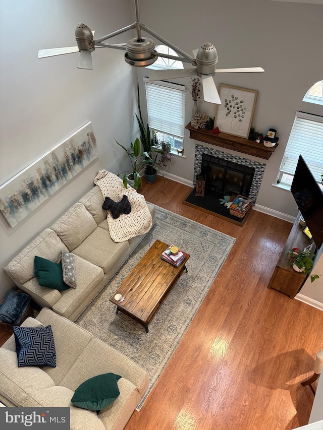 living room with a tile fireplace, ceiling fan, and wood-type flooring