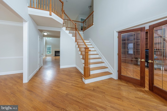 interior space featuring wood-type flooring, ornamental molding, a towering ceiling, and french doors