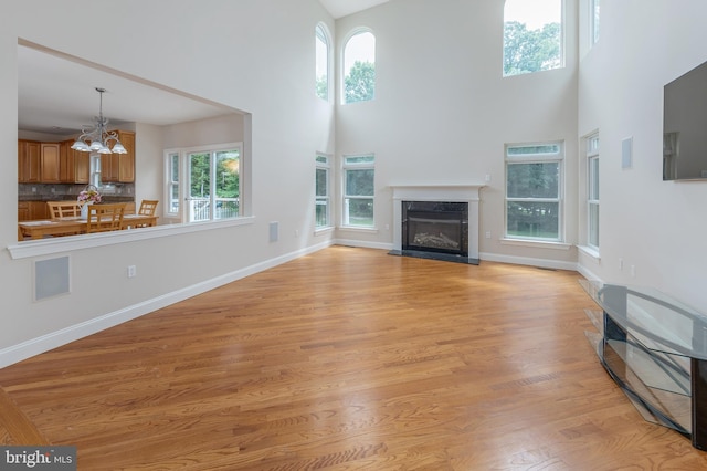 unfurnished living room featuring a fireplace, a towering ceiling, light wood-type flooring, and an inviting chandelier