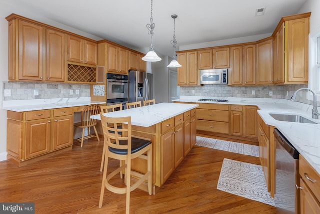 kitchen featuring sink, a center island, stainless steel appliances, hardwood / wood-style floors, and decorative light fixtures