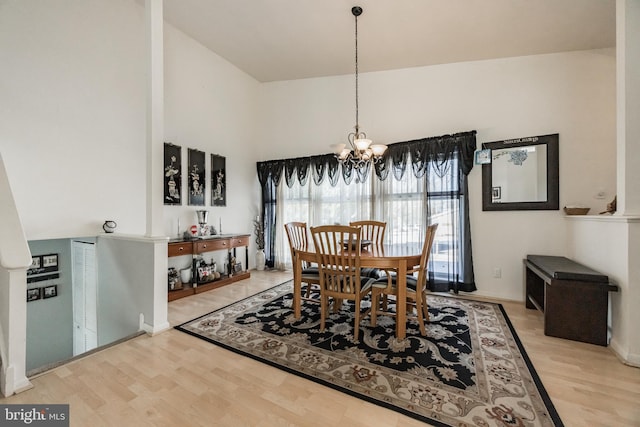 dining space featuring light hardwood / wood-style flooring, high vaulted ceiling, and an inviting chandelier