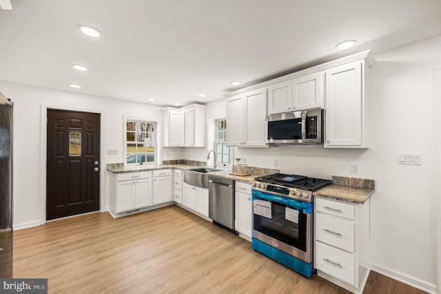 kitchen with sink, appliances with stainless steel finishes, light stone counters, white cabinets, and light wood-type flooring