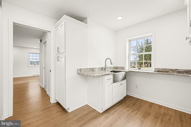 kitchen featuring white cabinetry, sink, light stone counters, and light wood-type flooring