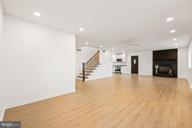 unfurnished living room featuring a brick fireplace, light hardwood / wood-style flooring, and ceiling fan