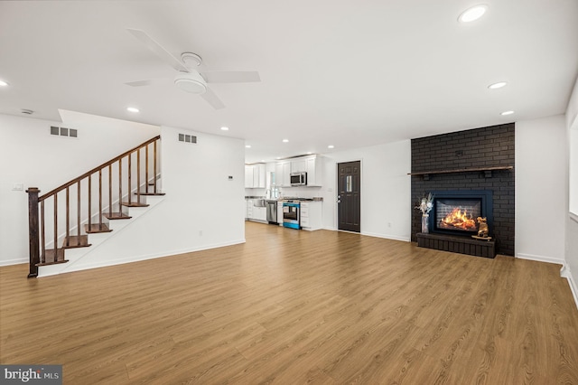 unfurnished living room with ceiling fan, light hardwood / wood-style floors, and a brick fireplace